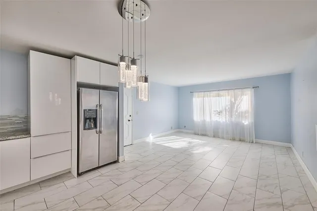 a view of an empty room and window cabinet and refrigerator in a kitchen