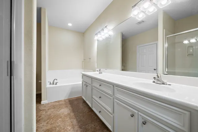 a spacious bathroom with a bathtub double sink and mirror