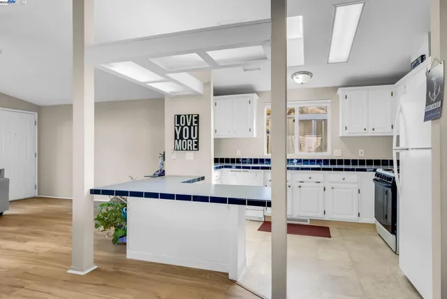 a large white kitchen with kitchen island a stove a sink dishwasher and white cabinets with wooden floor