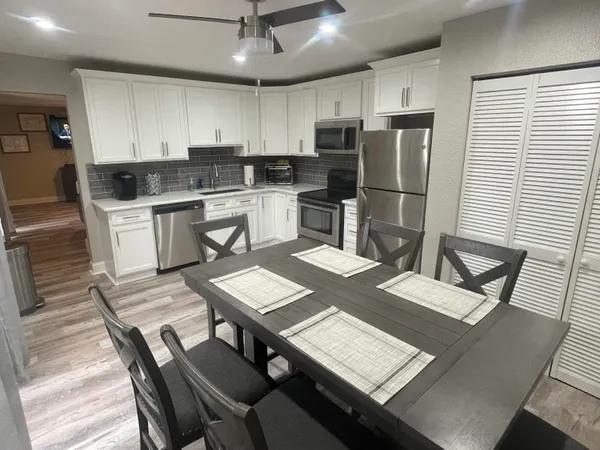 a kitchen with a refrigerator a stove a sink dishwasher a dining table and chairs with wooden floor