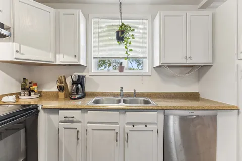 a kitchen with stainless steel appliances granite countertop a sink a window and white cabinets