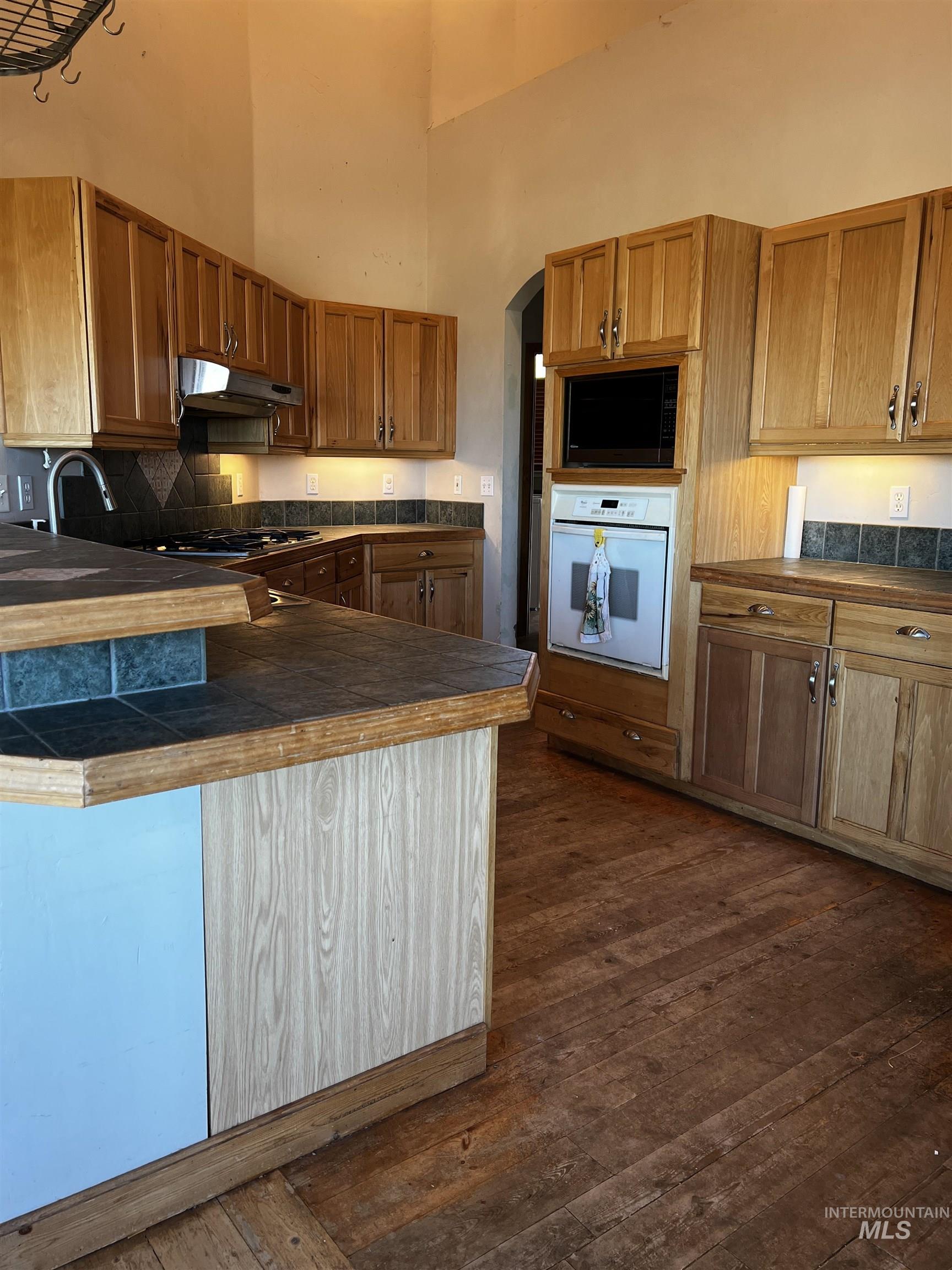 Wood-finish flooring, wood cabinetry, tile countertops, built-in wall oven, and built-in microwave