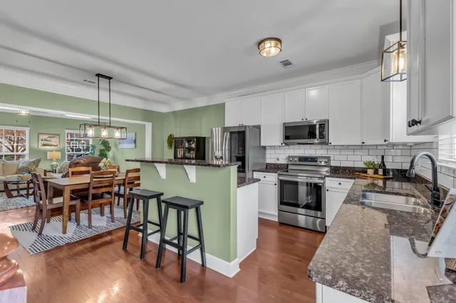 a kitchen with stainless steel appliances granite countertop a stove top oven a sink a dining table and chairs with wooden floor