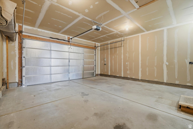 791 East Saddle Road Grantsville, UT 84029 - Photo 36 of 46 Spacious garage featuring a concrete floor, an overhead door with an automatic opener, exposed ceiling joists, and unfinished walls