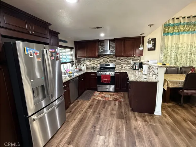 a kitchen with stainless steel appliances granite countertop a refrigerator a sink dishwasher a stove and white countertops with wooden floor