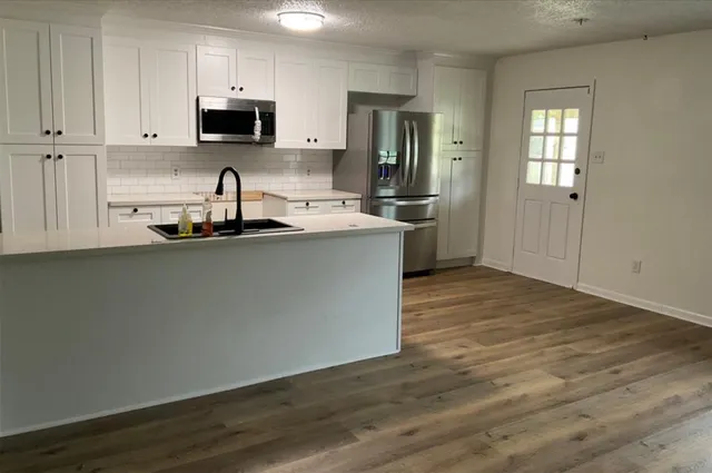 a kitchen with stainless steel appliances a sink dishwasher a refrigerator a stove top oven and a wooden floor