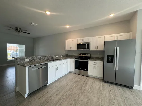 a kitchen with granite countertop stainless steel appliances a refrigerator cabinets and wooden floor