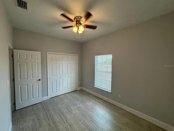 an empty room with wooden floor chandelier fan and windows