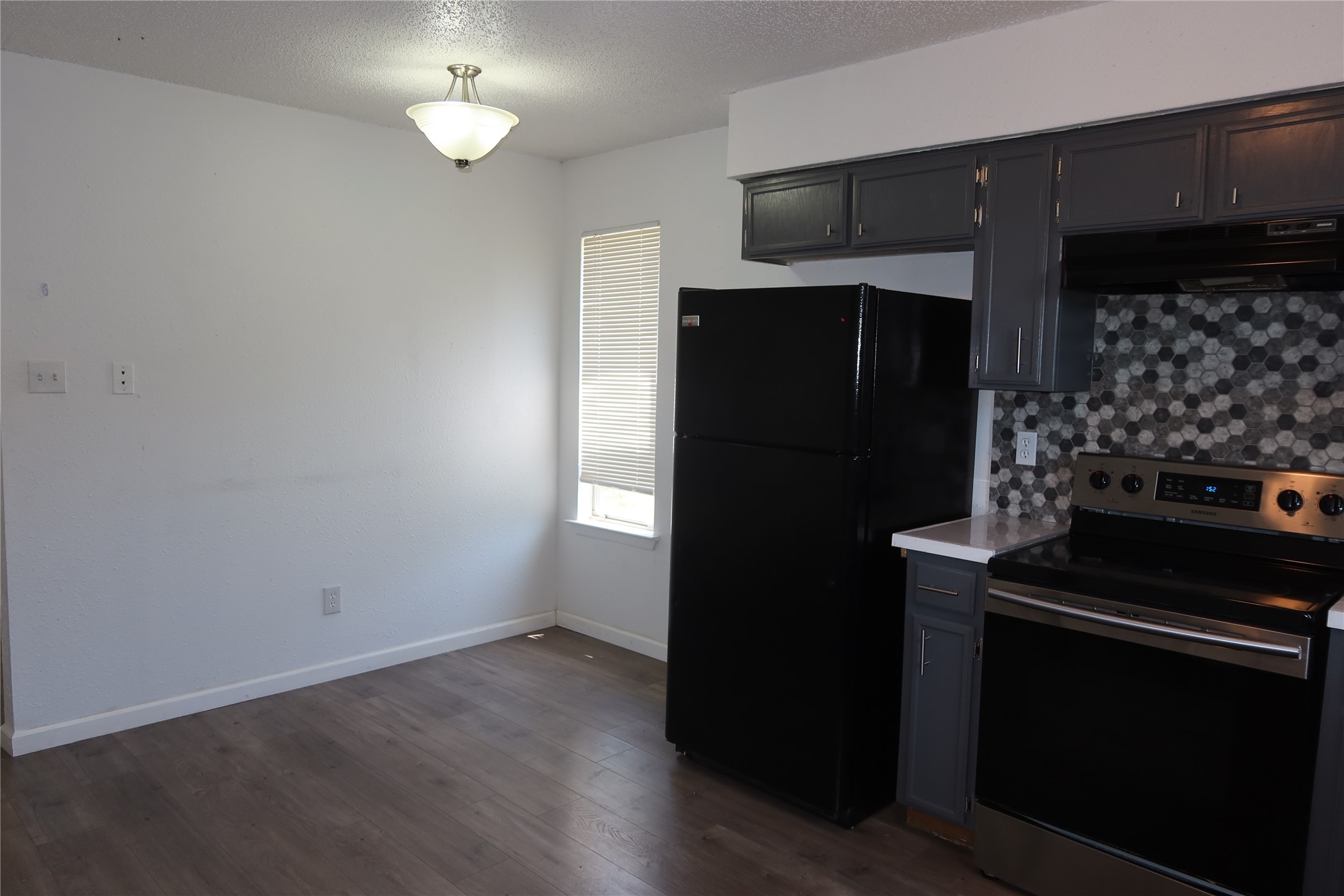 A windowed dining area sits adjacent to the functional kitchen with wood-look flooring.