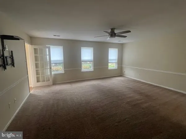 an empty room with chandelier fan and windows