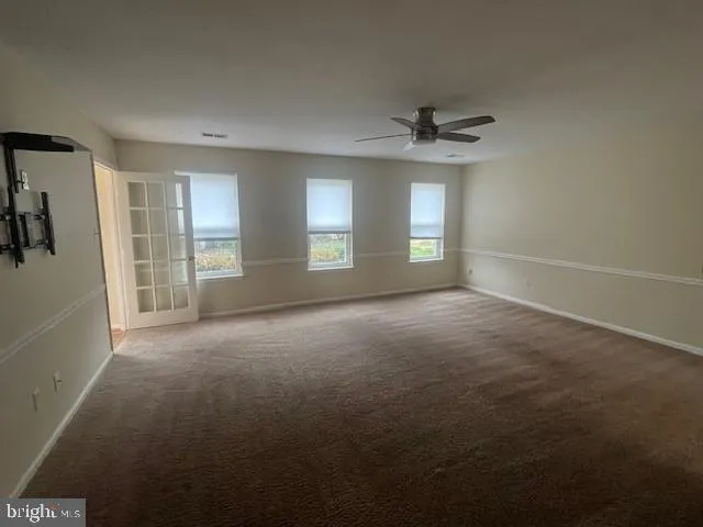 an empty room with chandelier fan and windows