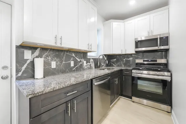 a kitchen with granite countertop a sink dishwasher a stove and a microwave oven with white cabinets