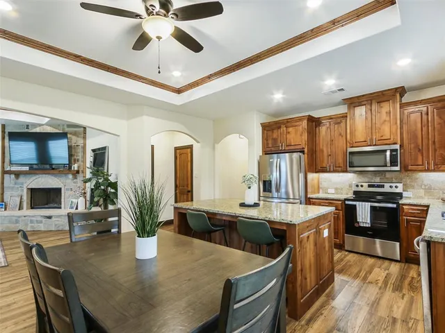 a kitchen with stainless steel appliances kitchen island granite countertop a stove top oven a sink a dining table and chairs with wooden floor