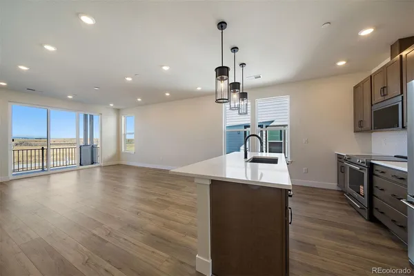 a room with stainless steel appliances kitchen island granite countertop a sink a stove and a wooden floors