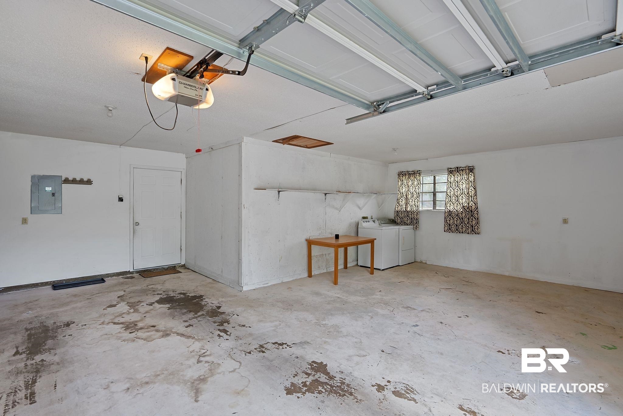 716 North Cedar Street Foley, AL 36535 - Photo 21 of 25 Spacious garage interior featuring an overhead garage door mechanism, white painted walls, a utility door, and a dedicated laundry area with window