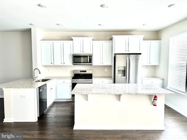 a kitchen with stainless steel appliances granite countertop a stove a sink a refrigerator a microwave oven and white cabinets with wooden floor