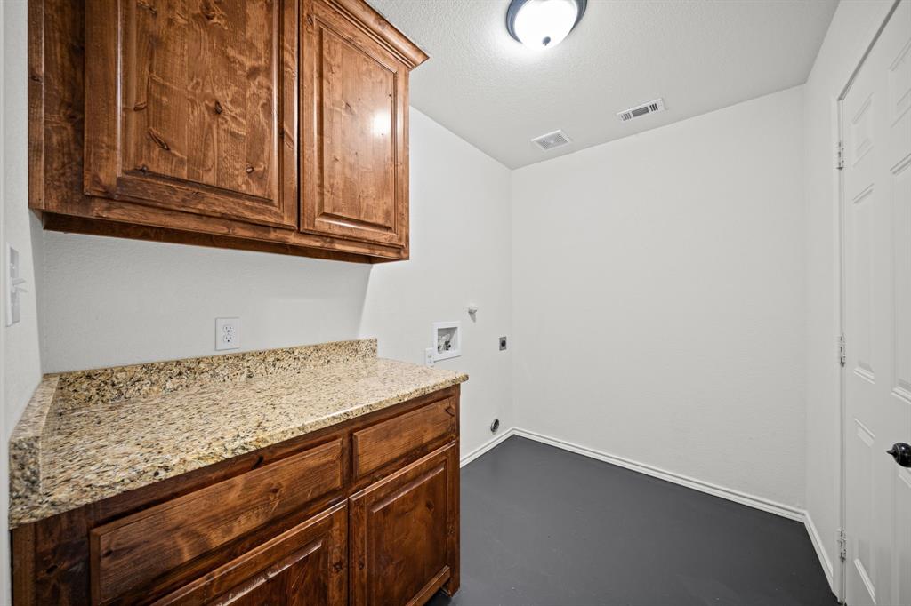 229 Firefly Drive Springtown, TX 76082 - Photo 22 of 33 Functional utility room featuring wood-finish cabinetry, granite-style countertops, and durable flooring