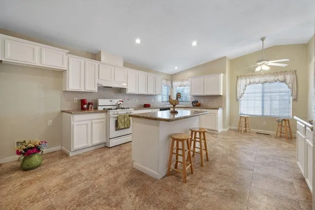 a kitchen with granite countertop a sink a stove a window cabinets and a counter top space