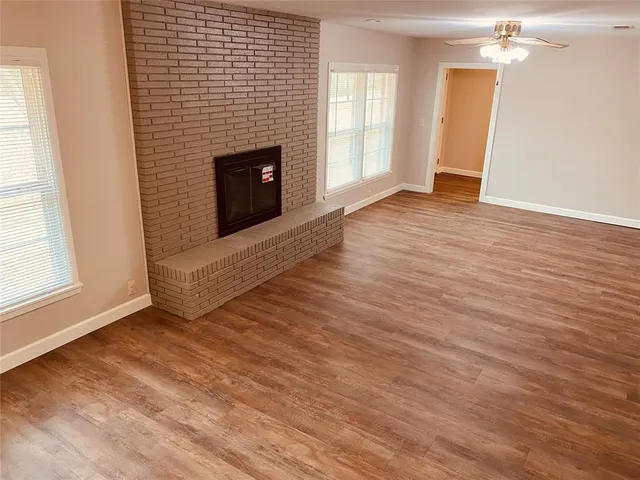 an empty room with wooden floor fireplace and windows