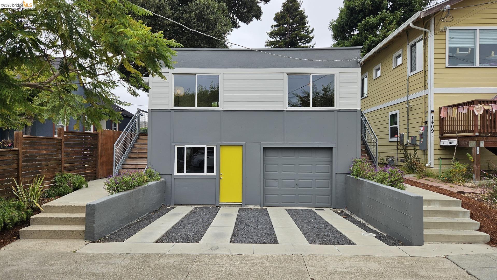 Modern two-story facade featuring a vibrant yellow entry door, an integrated garage, and a concrete driveway with dark aggregate strips