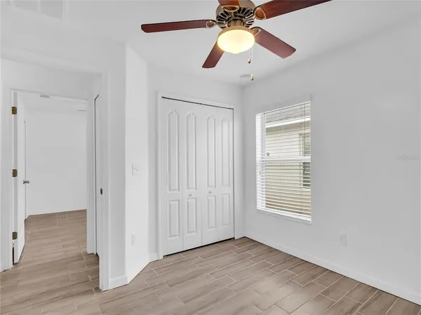 an empty room with wooden floor chandelier fan and windows