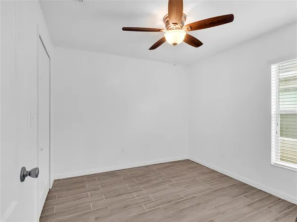 an empty room with wooden floor fan and windows