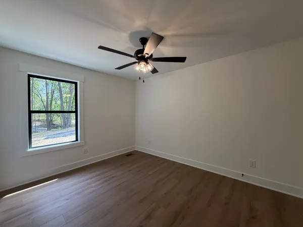 an empty room with wooden floor ceiling fan and windows