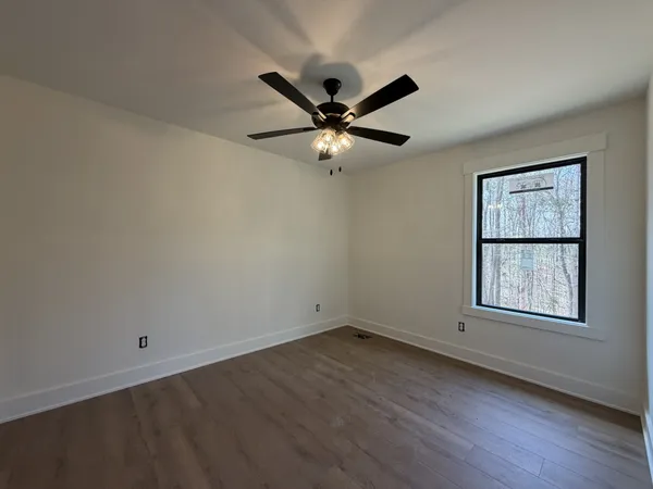 an empty room with wooden floor ceiling fan and windows