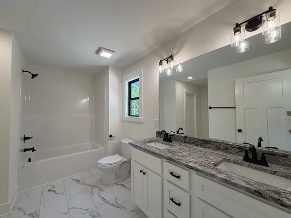 a bathroom with a granite countertop sink a toilet a large mirror and shower