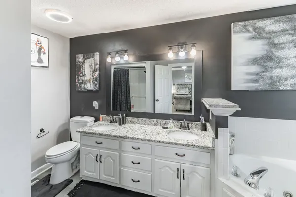 a bathroom with a granite countertop sink toilet and painting on the wall
