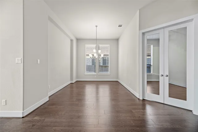 an empty room with wooden floor chandelier and windows