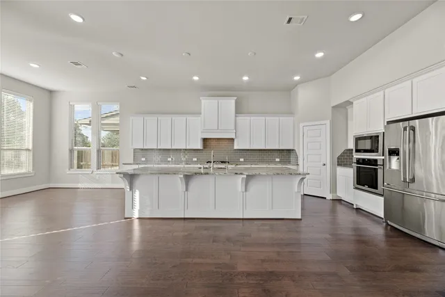 a large kitchen with stainless steel appliances granite countertop a large counter top a stove a sink and a refrigerator