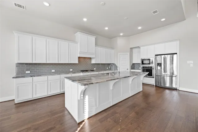 a large kitchen with stainless steel appliances granite countertop a stove a sink a refrigerator and white cabinets with wooden floor