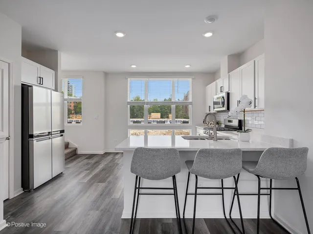 a kitchen with stainless steel appliances a dining table chairs refrigerator and sink