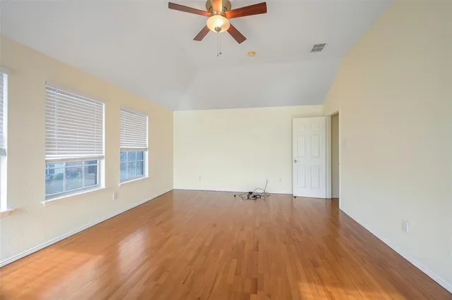 an empty room with wooden floor fan and windows
