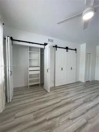 a view of an empty room with wooden floor closet and windows
