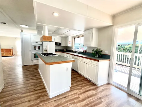a kitchen with stainless steel appliances a stove a sink dishwasher a refrigerator white cabinets with wooden floor