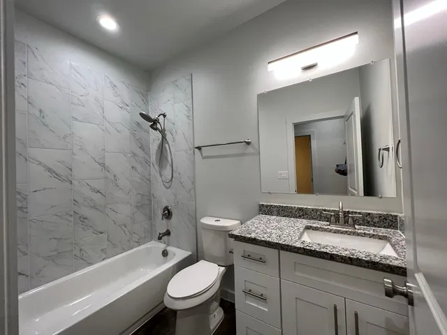 a bathroom with a granite countertop sink toilet mirror and bathtub
