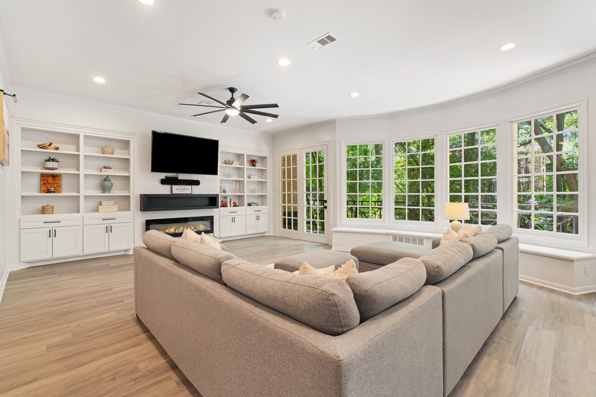 201 Vanderpool Lane, Unit 137 Houston, TX 77024 - Photo 2 of 42 Rare first floor living room is framed by a wall of windows overlooking lush greenery, filling the space with natural light and offering a peaceful tree-lined view. Custom built-ins, a sleek fireplace, and balcony access add to the rooms warm, elevated feel.