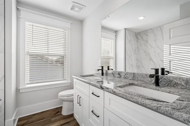 a bathroom with a granite countertop sink toilet a large mirror next to a window