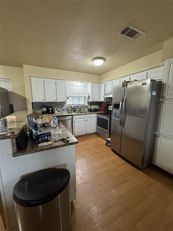 636 East Kempner Street Mabank, TX 75147 - Photo 22 of 28 Kitchen featuring white cabinetry, stainless steel appliances, wood-finish flooring, granite-style countertops, and a built-in kitchen island