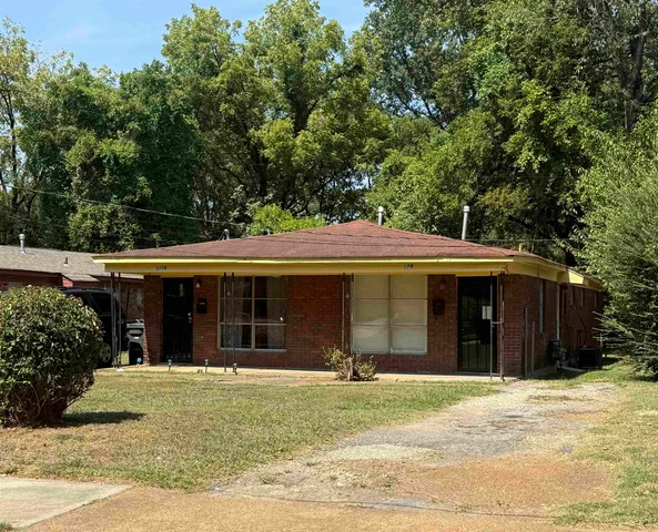 a view of a house with a yard plants and large tree
