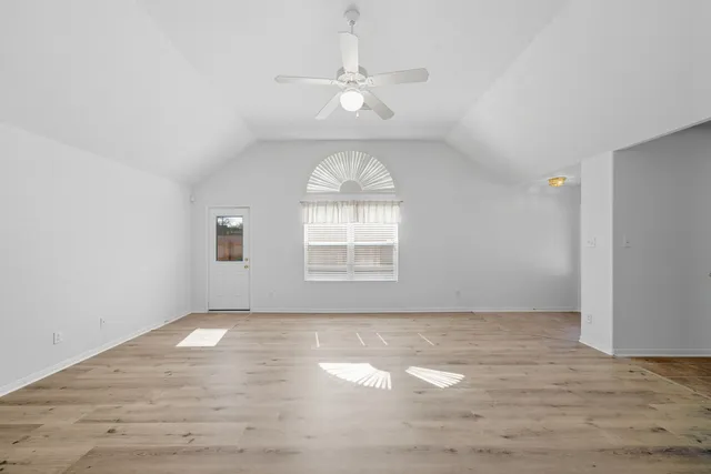 an empty room with wooden floor window and ceiling fan
