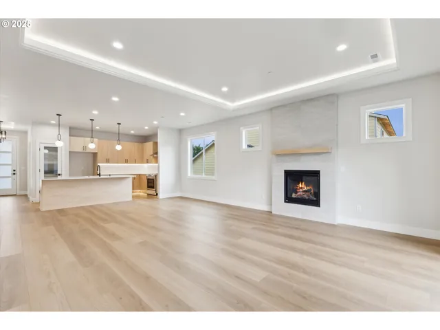 a view of an empty room with a fireplace and kitchen view