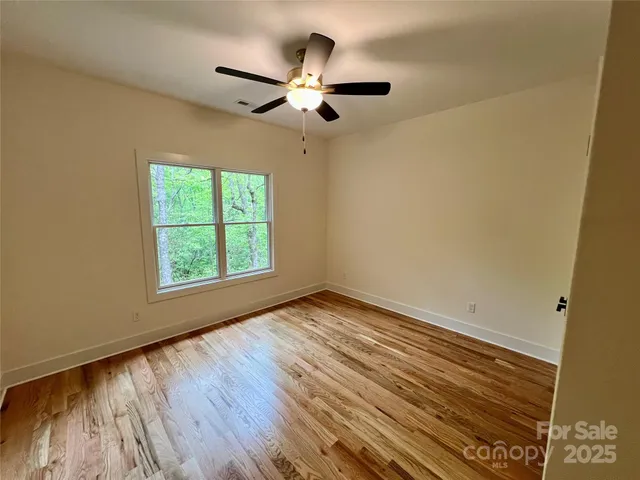 an empty room with wooden floor chandelier fan and windows