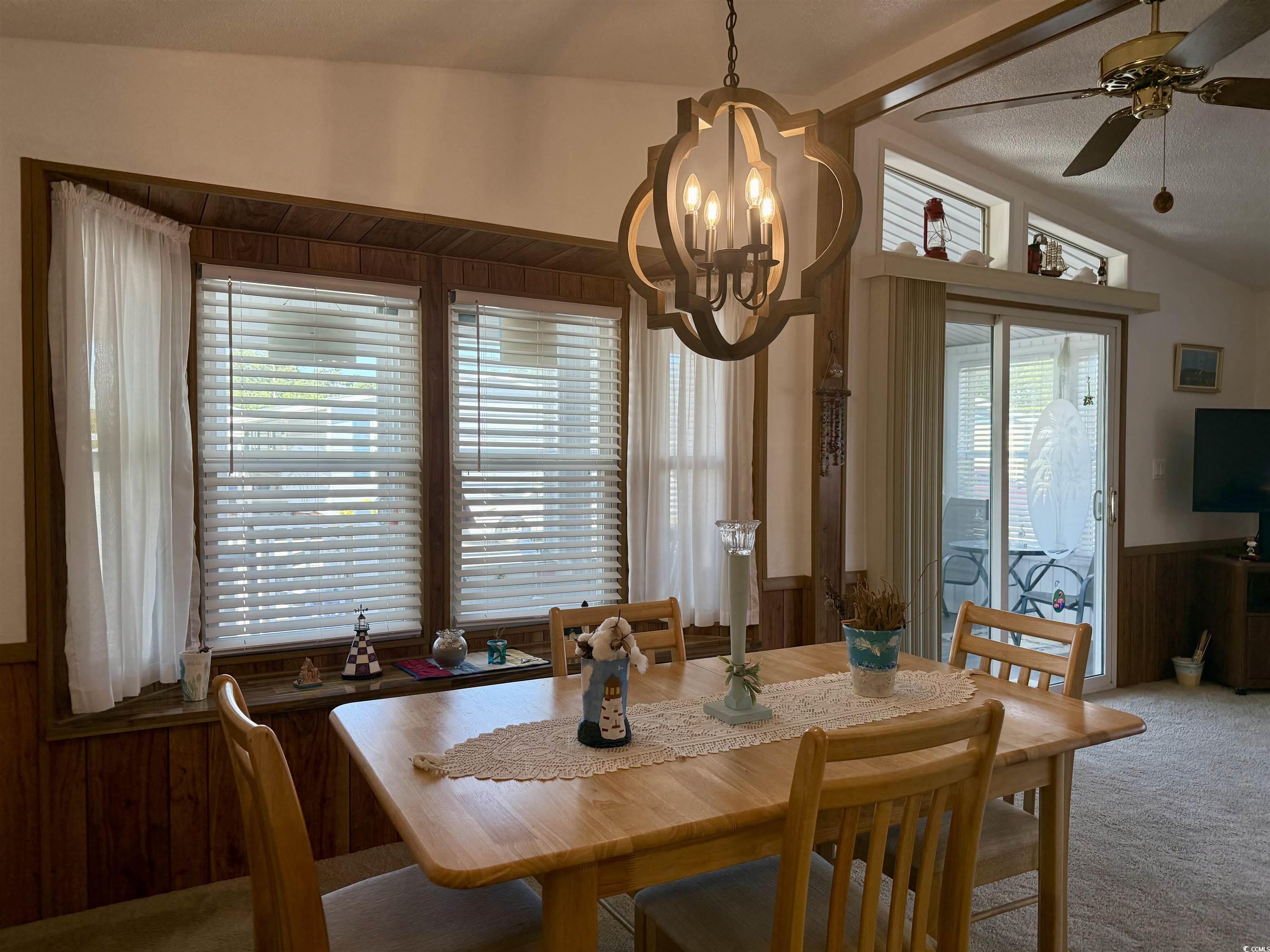 505 Sandpebble Surfside Beach, SC 29575 - Photo 4 of 27 Carpeted dining area with healthy amount of natural light, a chandelier, wainscoting, a ceiling fan, and wood walls