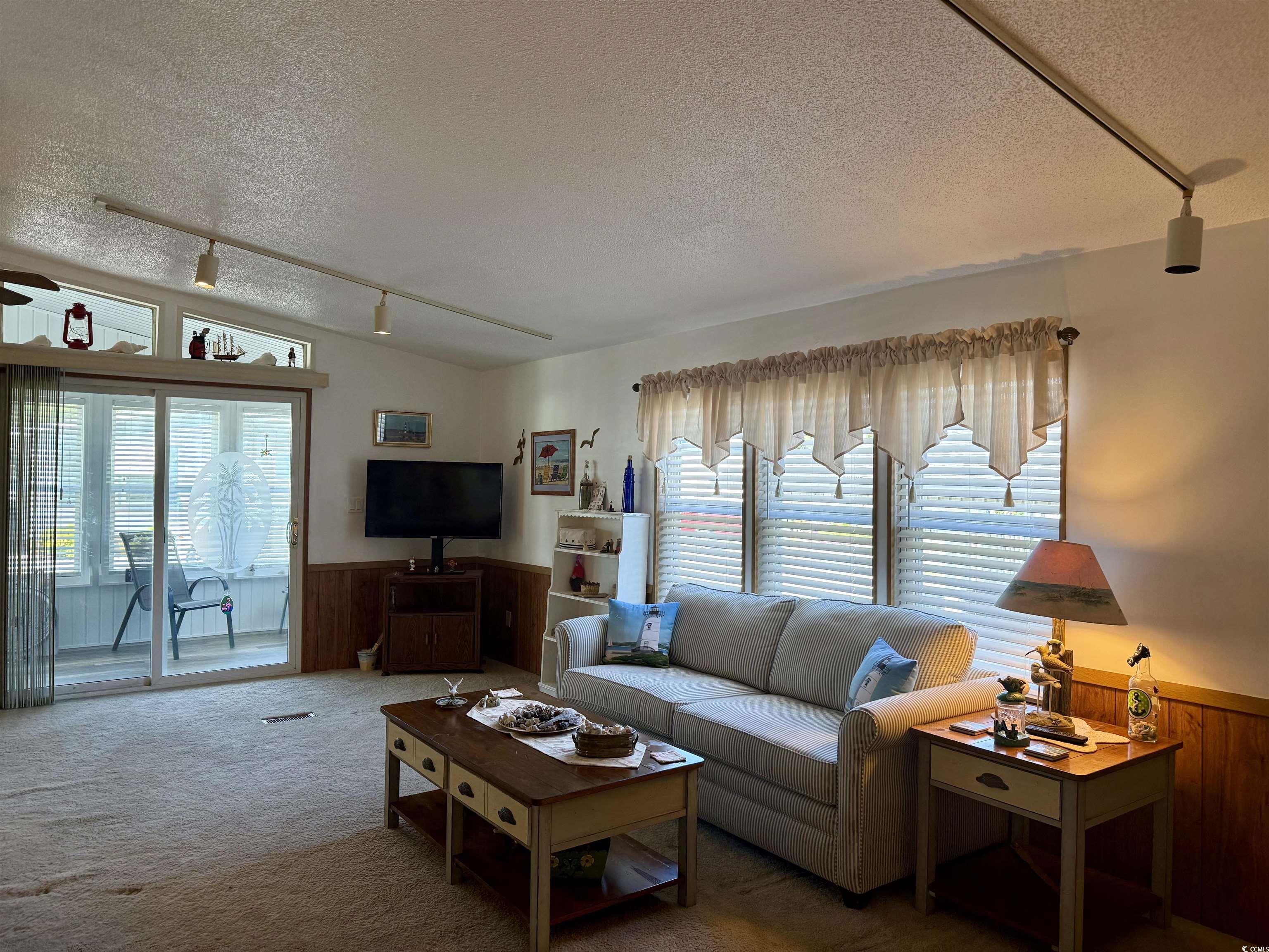 505 Sandpebble Surfside Beach, SC 29575 - Photo 6 of 27 Carpeted living room featuring track lighting, a textured ceiling, wainscoting, and wooden walls