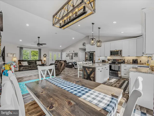 a kitchen with stainless steel appliances kitchen island granite countertop a refrigerator a stove a sink a dining table and chairs with wooden floor