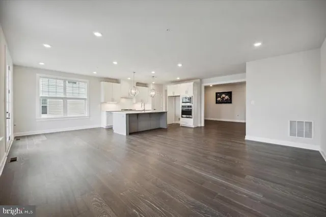 a view of empty room with wooden floor and kitchen