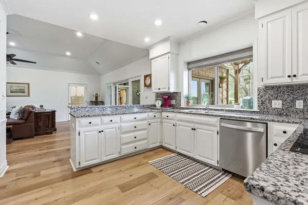 a large white kitchen with granite countertop a stove a sink a dining table and chairs